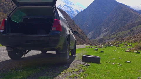 Black car in process of changing flat tire at mountains during sunny spring day Stock Footage 274051292