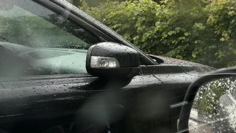 Black car side mirror covered in raindrops viewed through a wet window during a Stock Photos