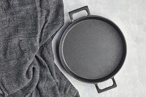 Black cast iron empty frying pan and gray kitchen towel on a gray concrete Stock Photos