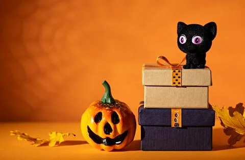 Black cat on stacked gift boxes beside jack-o-lantern on orange background .. 写真素材