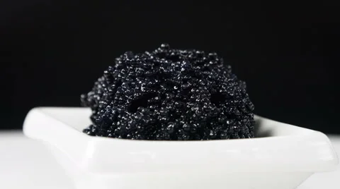 Black caviar in a small dish on a black background, close-up rotation. Video stock 63534645