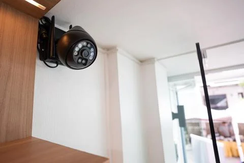 A black CCTV security camera installed beside a wooden wall near a mirror d.. Stock Photos
