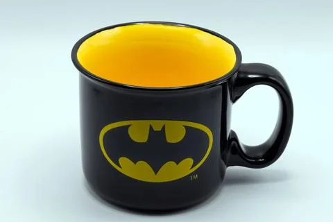 A black ceramic coffee mug featuring the iconic batman bat logo. Stock Photos