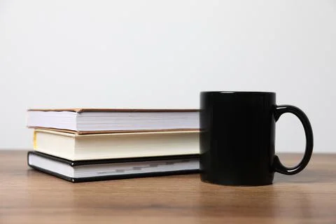 Black ceramic mug and stack of books on wooden table Stock Photos