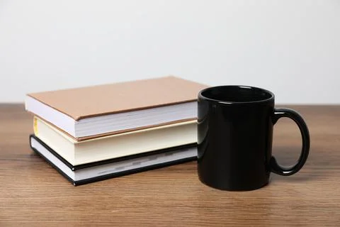 Black ceramic mug and stack of books on wooden table Stock Photos
