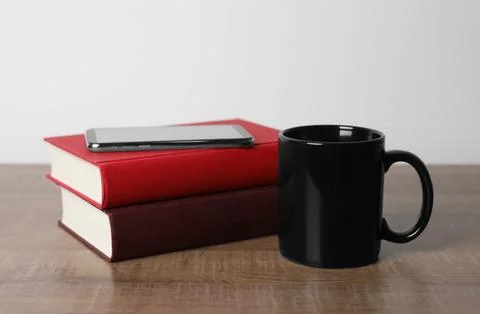Black ceramic mug, stack of books and smartphone on wooden table Stock Photos
