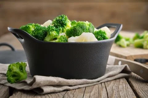 Black ceramic saucepan with cooked broccoli and cauliflower on kitchen table. Stock Photos