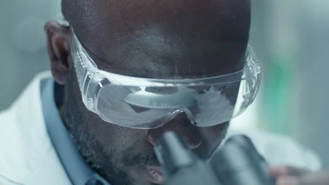 Black Chemist in Safety Glasses Looking through Microscope in Laboratory Stock Footage 275477954