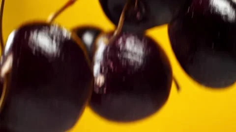 Black cherries fly on a yellow background closeup in slow motion Stock Footage 150768004