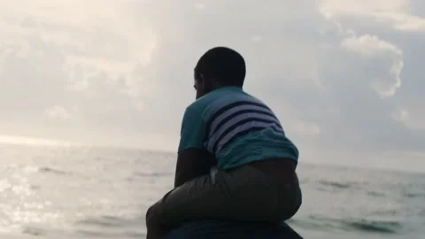 Black child on dads shoulders while they watch the ocean horizon. 4K. Stock Footage 154050629