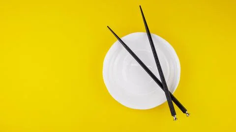 Black chopsticks for sushi in a white saucer on a yellow background, isolated Stock Photos