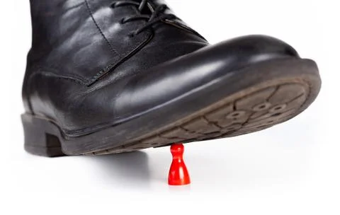 Black classy boot stomping and crushing a small red pawn game piece Stock Photos