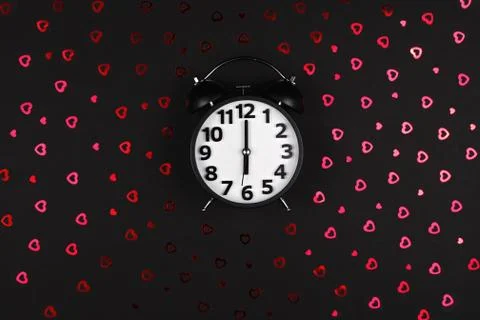 Black clock alarm clock on a black background of sequin hearts Valentines day Stock Photos