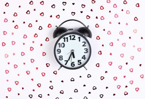 Black clock alarm clock on a white background of sequin hearts Valentines day Stock Photos