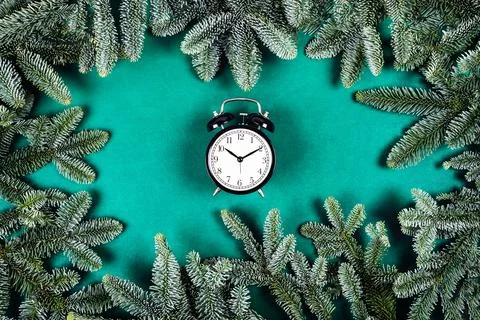 Black clock on green background with Christmas branches. Stock Photos