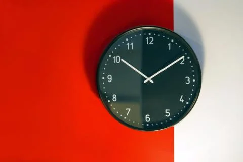 Black clock on a red and white wall with shadows Stock Photos
