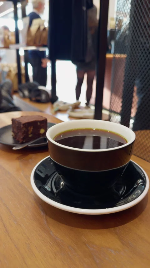Black coffee in ceramic cup with brownie dessert on wooden table inside modern Stock Footage 346853783