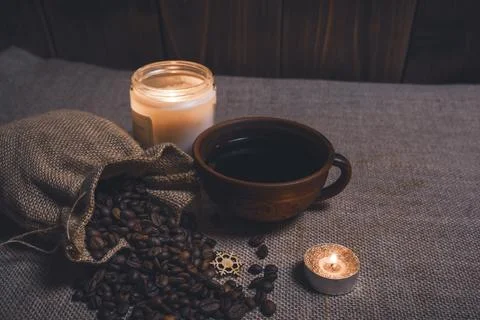 Black coffee in a ceramic cup with burlap sack of beans and glowing candles Stock Photos