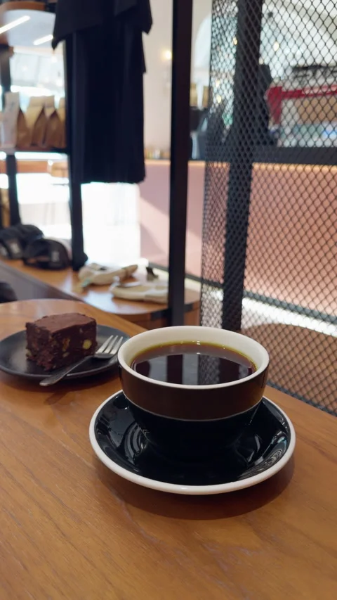 Black coffee in ceramic cup with dessert slice on wooden cafe table beside Stock Footage 346853787