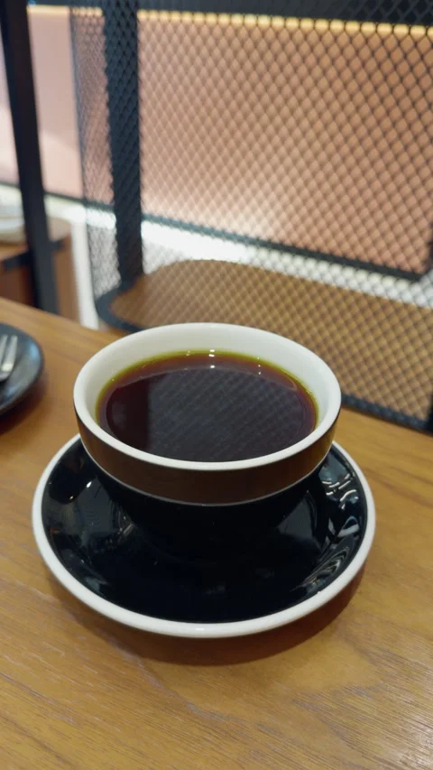 Black coffee in ceramic cup on saucer at wooden cafe table beside mesh partition Stock Footage 346853792