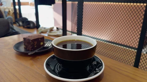 Black coffee cup on wooden table with chocolate cake in cozy cafe setting Stock Footage 346853785
