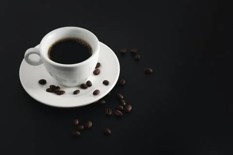 Black coffee in white coffee cup and saucer with beans coffee on black backgr Stock Photos