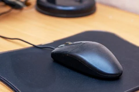 A black colored computer mouse is currently resting on a black mouse pad Stock Photos