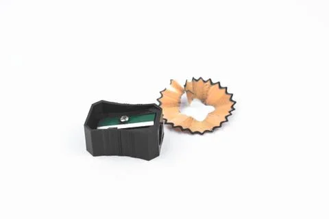 Black colored plastic pencil sharpener and a piece of pencil shavings placed Stock Photos
