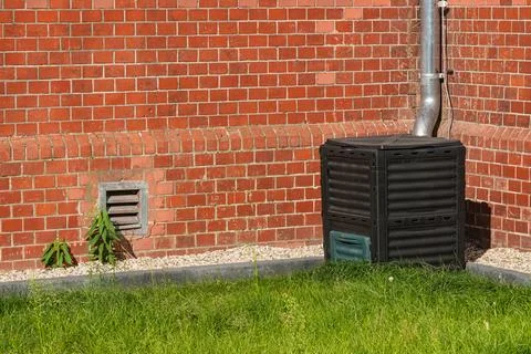 Black compost bin next to brick wall in a garden area Stock Photos