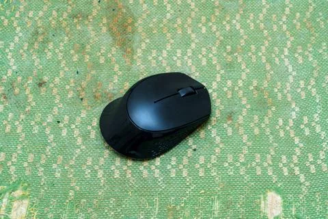 Black computer mouse on a green textured surface in a bright room Stock Photos