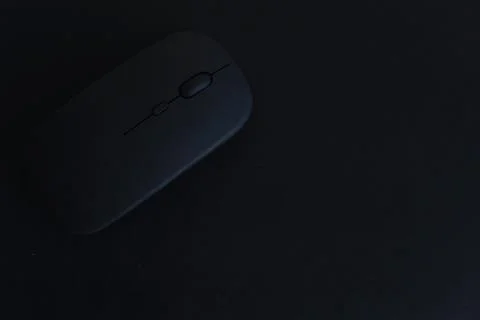 A black computer mouse sits on a dark surface Stock Photos