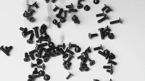 Black computer screws fall on white surface and collect in pile for device Stock Footage 346876442