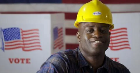Black contractor puts on hard hat with "I Voted" sticker at polling station Stock Photos