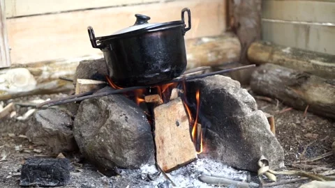 A black cooking pot placed on a traditional open-fire stone stove with burning Stock Footage 344093901