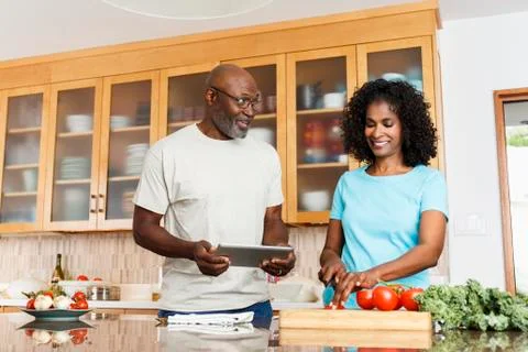 Black couple with digital tablet chopping tomatoes in kitchen Stock Photos