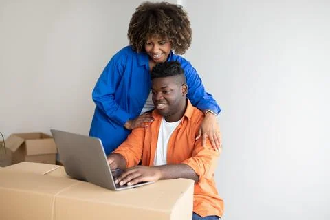 Black Couple Using Laptop After Moving Home, Checking Interior Ideas In Internet 写真素材