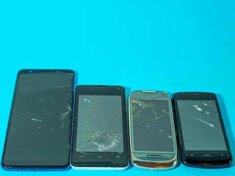 Black crashed smartphone with broken screen and body on a blue table in service. Stock Photos