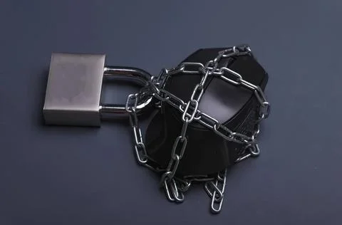 Black cube locked with silver chain and padlock on dark surface Stock Photos
