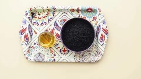 Black cumin seeds and black cumin oil are displayed on a colorful patterned.. Video stock 332323907