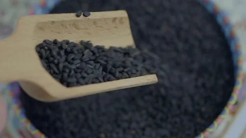 Black cumin seeds being poured from wooden scoop into decorative bowl in cl.. Video stock 332407900