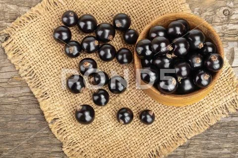 Black currants in bowl on burlap and wooden background.Top view. Flat lay Stock Photos