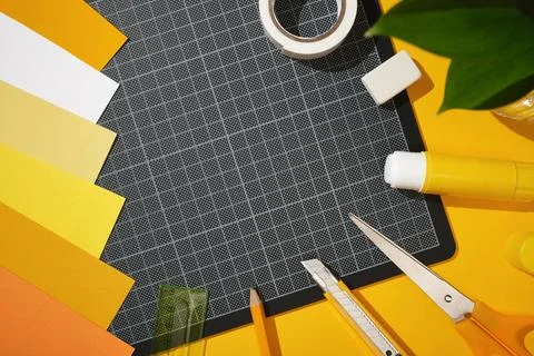 A black cutting mat surrounded by craft supplies. Glue, scissors, a pencil,.. Stock Photos