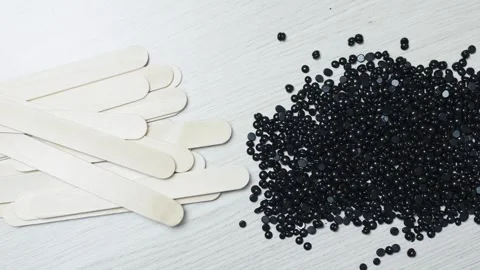 Black depilation hard wax beans scattered near wooden spatulas on rustic wooden Stock Footage 311117396