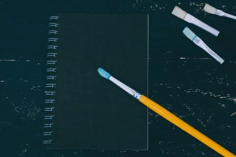 Black desk with black notepad and watercolour brushes Stock Photos