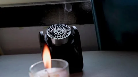 Black Diffuser Emitting White Vapor Behind Lit Candle Stock Footage 346456976