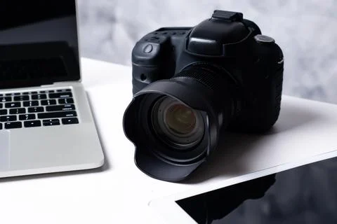 A black digital camera, a tablet and a computer laptop on a table. Stock Photos