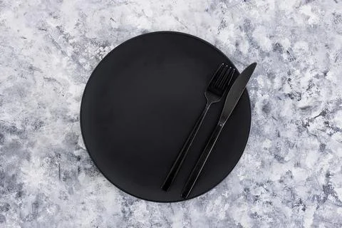 Black dining plate with fork and knife on gray background with minimalist com Stock Photos