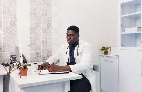 A black doctor takes notes while working online from the clinic, consults pat Stock Photos