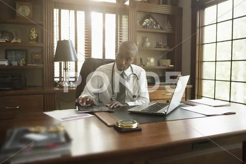 Black Doctor Using Digital Tablet In Office