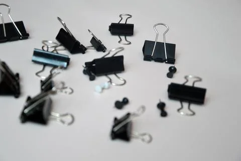 Black document clips and buttons loosely scattered on a white background. Off Stock Photos